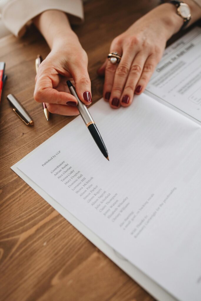 A person pointing at a printed document with a pen on a wooden desk, symbolizing attention to detail.